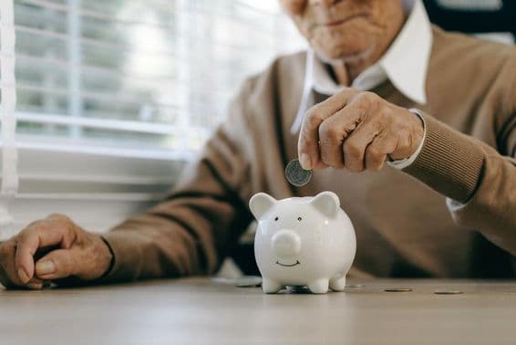 Saving money, elderly man placing coins into a piggybank