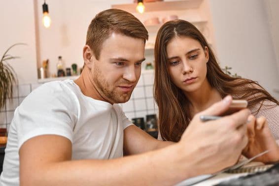 Young couple enjoying coffee in kitchen while reading an online banking notification on a mobile phone.