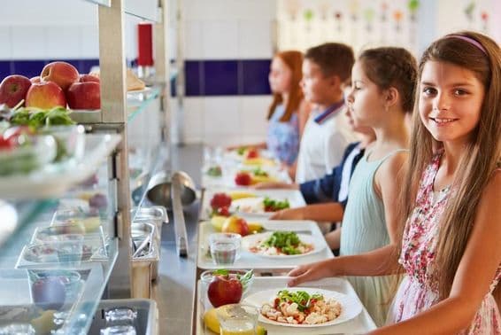 Smiling girl with food tray, standing in line with friends during lunch break at the school cafeteria.