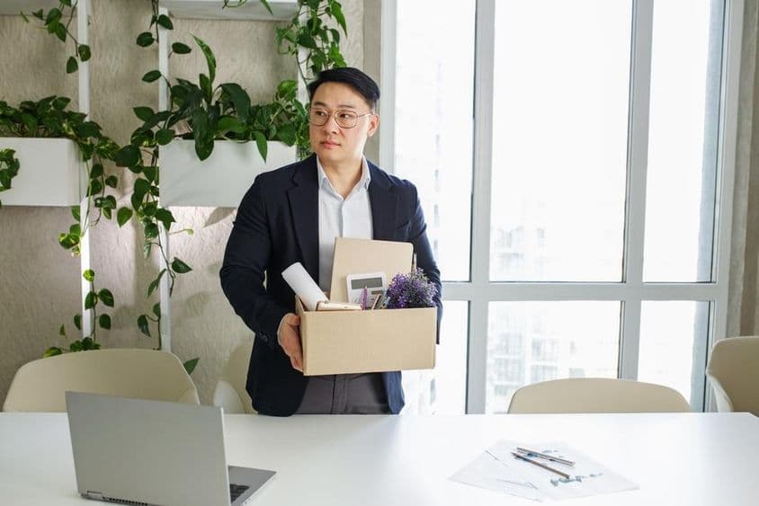 A man is being laid off from his workplace, packing his personal belongings into a cardboard box.