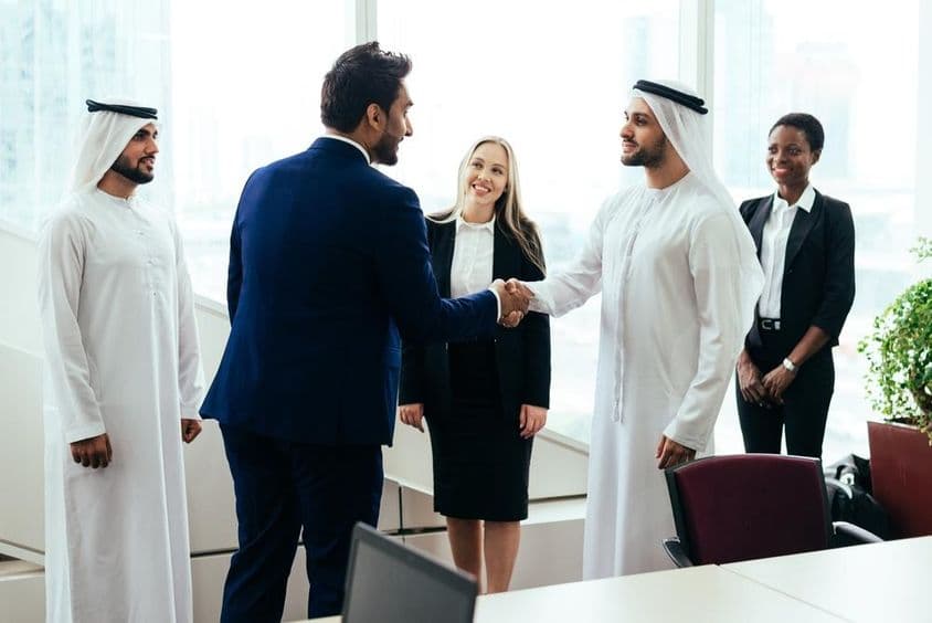 A multinational Western and Middle Eastern business team working together in a Dubai office.