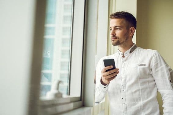 Businessman standing by a window, holding a smartphone.