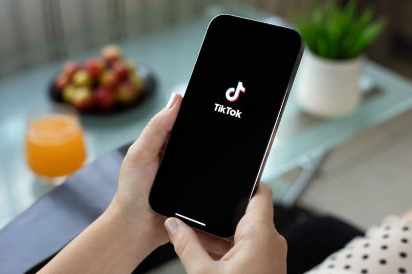 Apple iPhone 15 Pro Max in a woman's hand, TikTok video on screen.