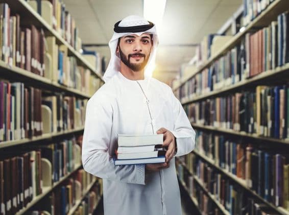 Arab student standing in library holding books.