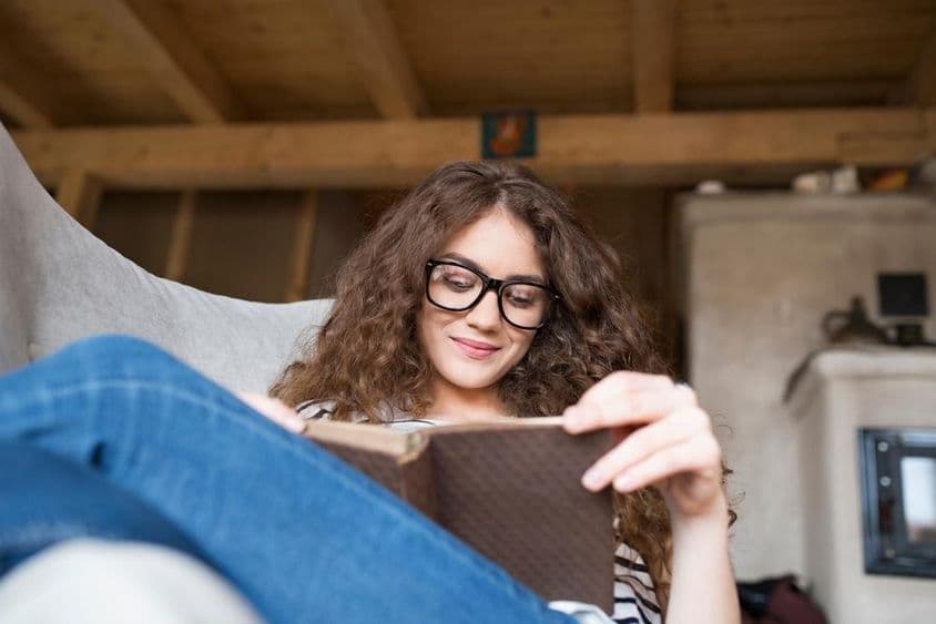 Schoolgirl sitting in an armchair reading a book.