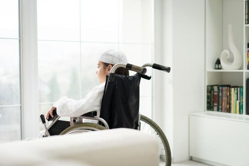 A young boy in a wheelchair looking through a window.