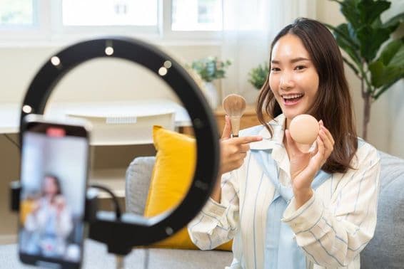 Young influencer woman blogger using smartphone speaking in a video streaming podcast.