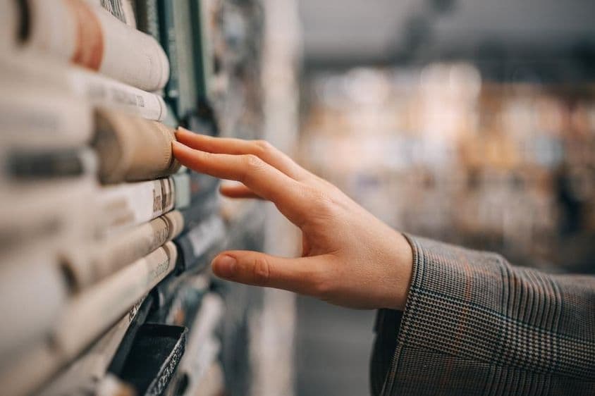 A hand touches the spine of an old book on a bookshelf.