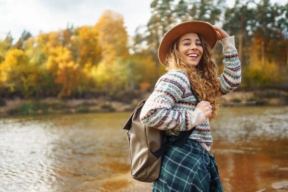 Female traveler with backpack and cap enjoying an autumn hike along a river.