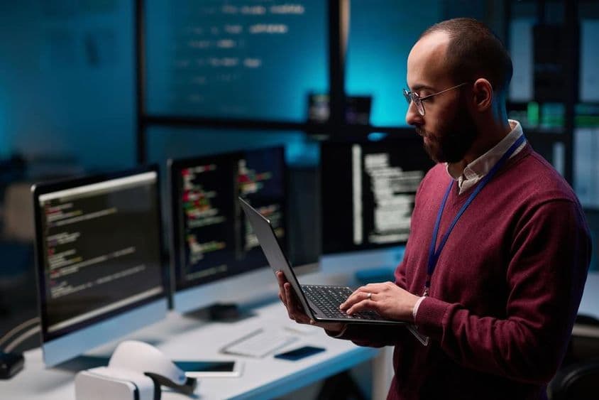 Computer programmer holding an open laptop in an IT and cybersecurity office.
