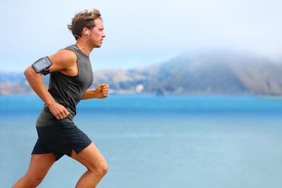 Male runner listening to music while jogging with a smartphone.