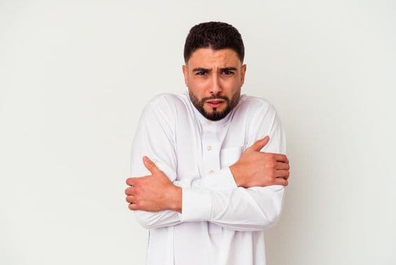 Young Arab man in traditional attire shivering from cold.