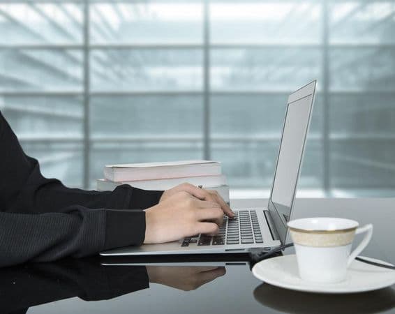 A woman working on a laptop with a coffee cup beside her.