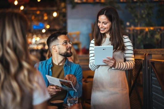 A smiling waitress takes an order at a cozy bar.
