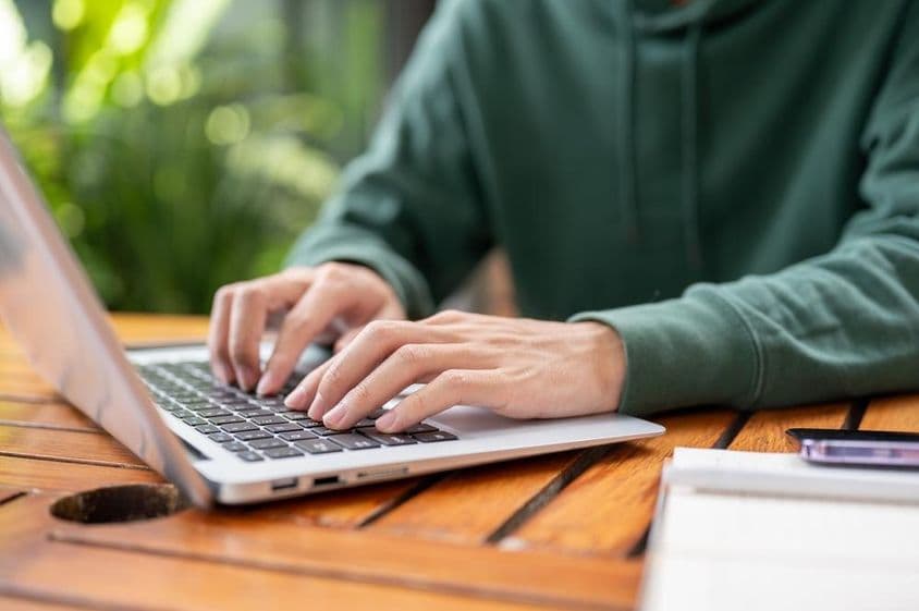 Man in green sweater working remotely on a laptop at an outdoor table.