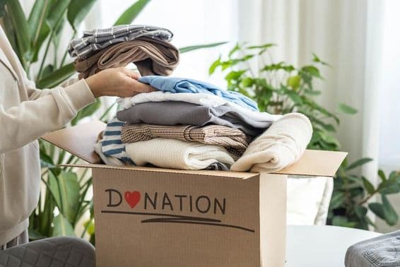 A woman at home placing clothes in a cardboard box for donation, for recycling.