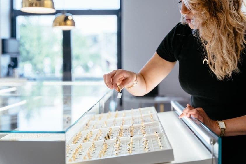A female jewelry vendor placing a gold ring on the jewelry store counter