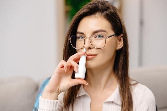 Young woman using a nasal spray to ease breathing.