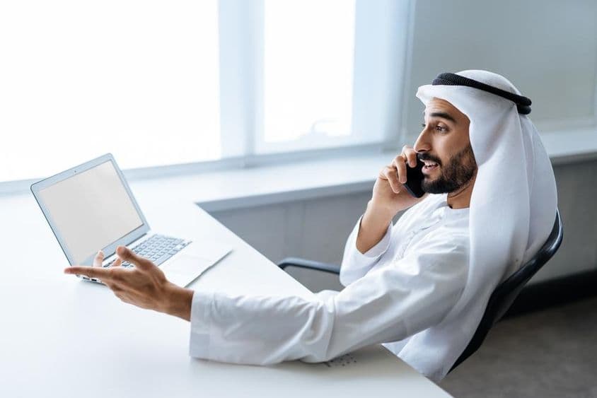 A successful businessman in traditional Emirati white attire working in Dubai.