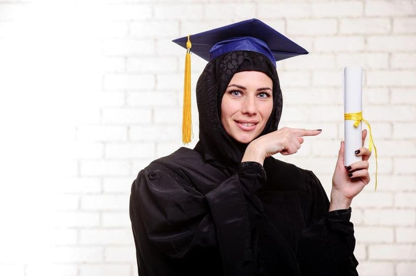 Happy Muslim graduate posing with diploma indoors.