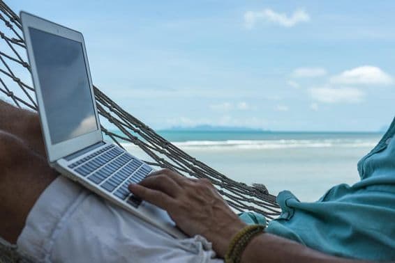A man working on a computer in a hammock with a laptop on Dubai's beach.