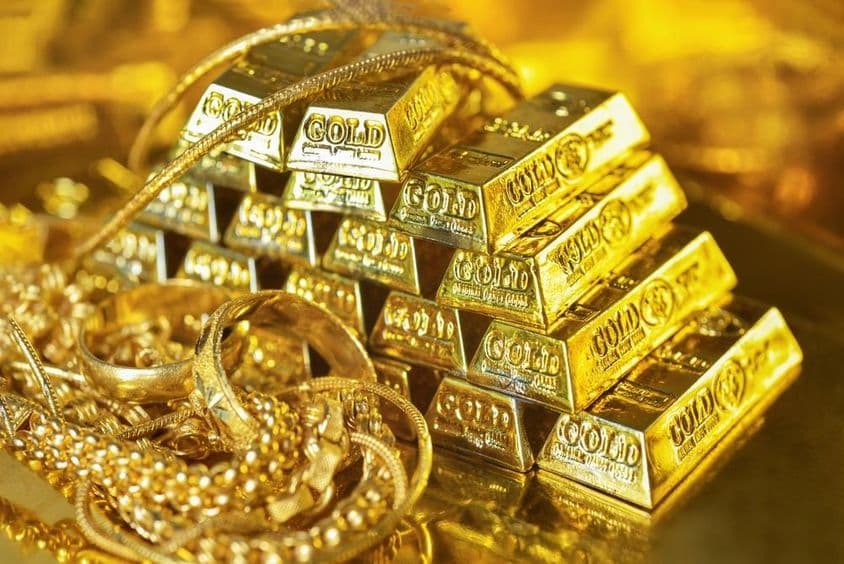 Gold bars and jewelry reflecting on a bright background.