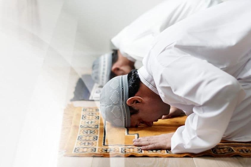 Islamic men dressed in white bowing in prayer.
