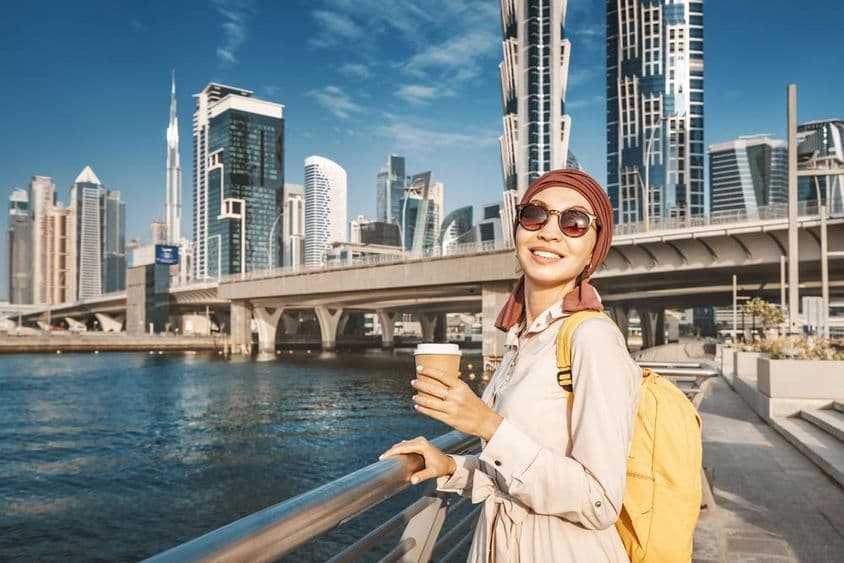 Muslim woman with a yellow backpack walking by Dubai canal.