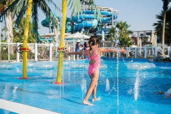 Little girl playing in a swimming pool with fountains in a water park.