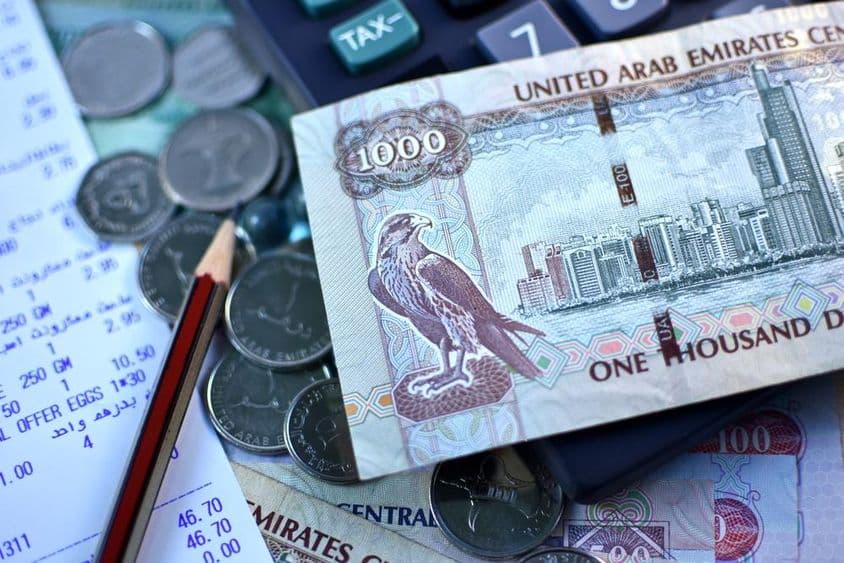 UAE 1000 dirham banknote and a handful of coins.