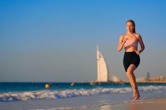 Young woman running on the beach in Dubai with Burj Al Arab Jumeirah in the background.