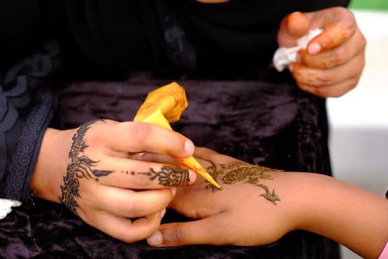 A girl applying henna design on another's hand.
