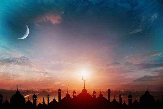 Mosque domes against a dusk blue sky with a crescent moon in the background.
