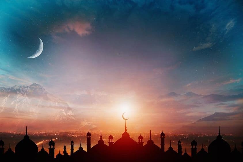 Mosque domes against a dusk blue sky with a crescent moon in the background.