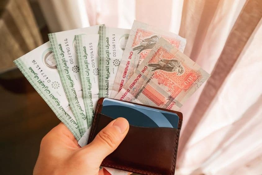 Dirham cash banknotes held with a wallet.