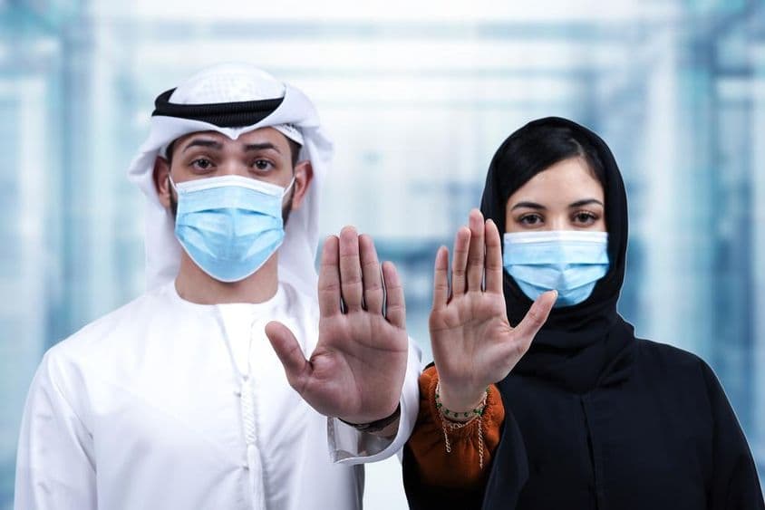 Arab man and woman wearing medical masks showing a stop gesture.