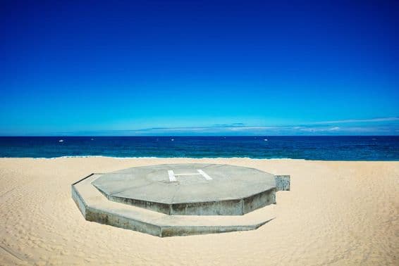 Helicopter landing on a sandy beach next to a blue ocean.