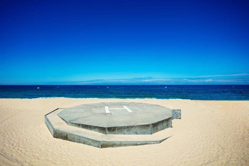 Helicopter landing on a sandy beach next to a blue ocean.
