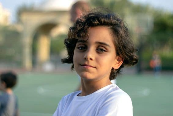 A cute little boy standing on a basketball court and smiling.