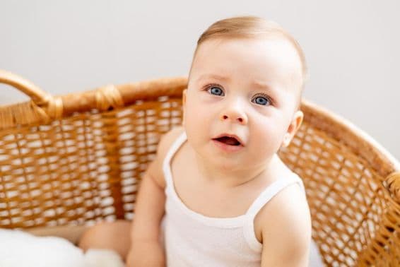 A baby in a woven cradle at home.