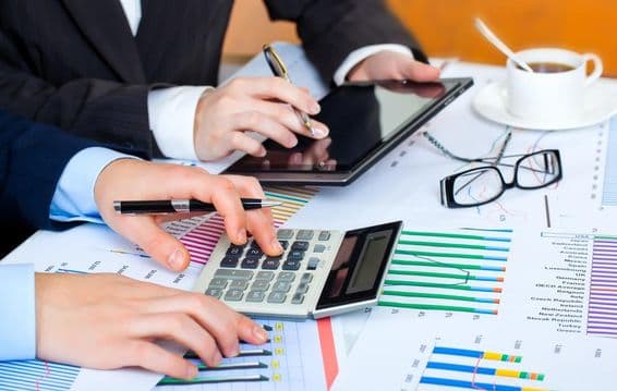 Graphs, calculator, tablet, diligent hands studying the data.