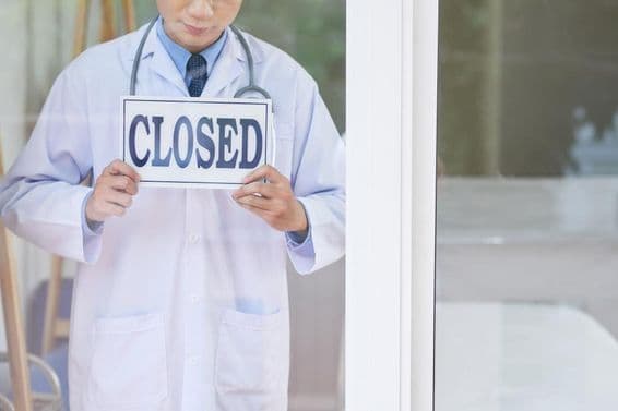 A man in a medical uniform holding a closed sign.