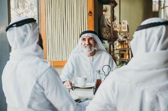Three businessmen enjoying tea in Dubai while wearing traditional Emirati attire.