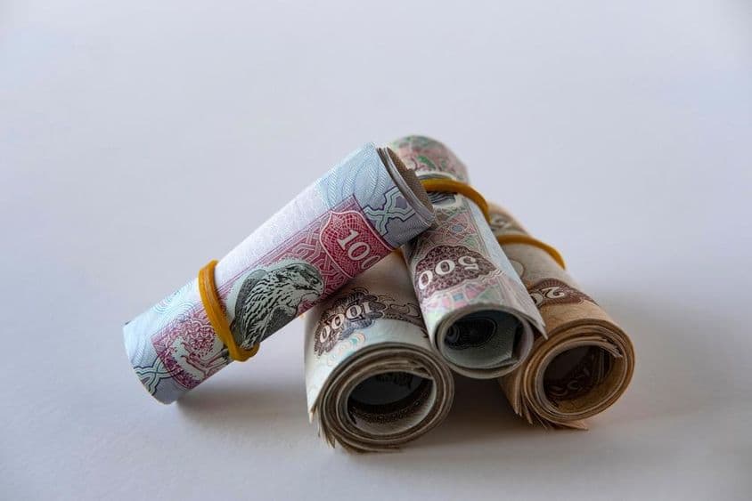 A collection of UAE dirham currency and coins rolled up and stacked.