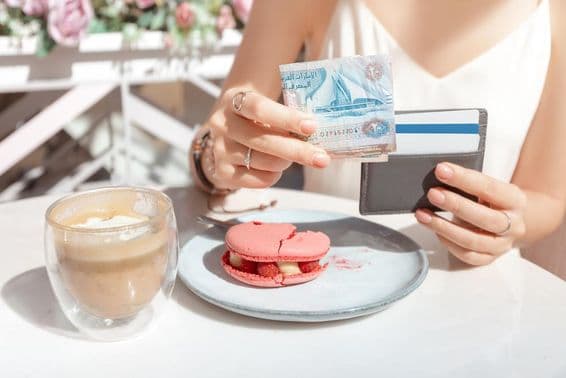 Girl paying for breakfast at a café in Dubai with dirhams.