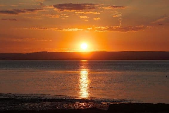 Sunset reflecting on water and clouds during the summer solstice.