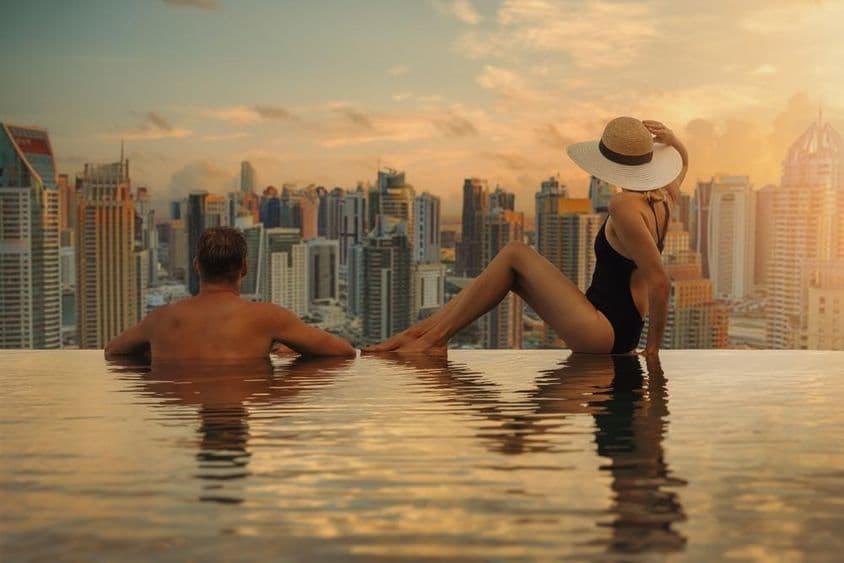 A couple enjoys Dubai's skyline with skyscraper architecture from an infinity pool at sunset.