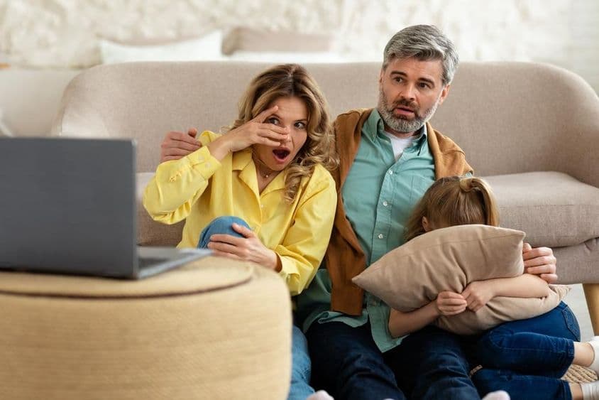 Shocked middle-aged parents and daughter in shock watching movie online on laptop.