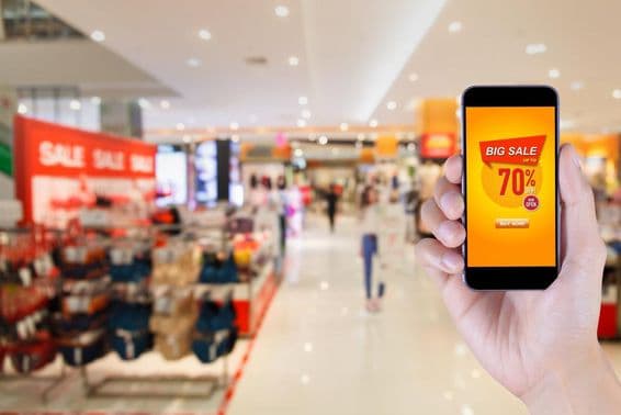 Smartphone displaying big sale app screen with blurred shopping mall background.