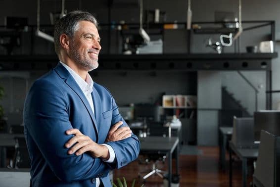 Businessman CEO in a suit stands in an office with crossed arms.